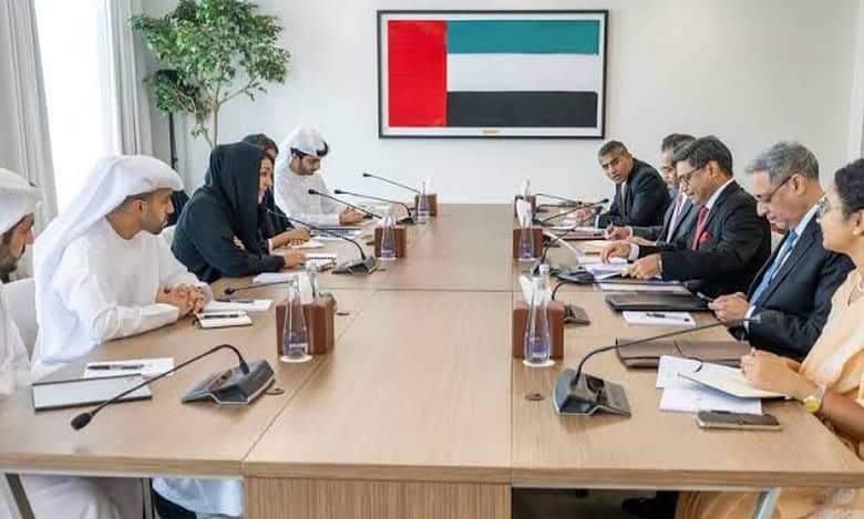 A group of delegates from India and the UAE engaged in a formal meeting, seated around a conference table with microphones, documents, and a UAE flag in the background.