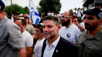 Israeli Finance Minister Bezalel Smotrich walking among a crowd with an Israeli flag in the background.