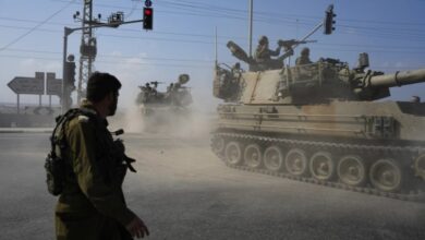 Israeli soldiers and armoured vehicles move through a dusty road junction under a traffic light in Gaza.