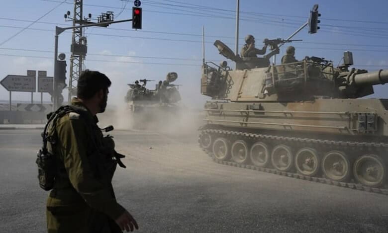 Israeli soldiers and armoured vehicles move through a dusty road junction under a traffic light in Gaza.