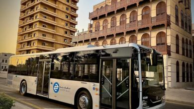 Modern Jeddah bus parked near traditional buildings in the city.