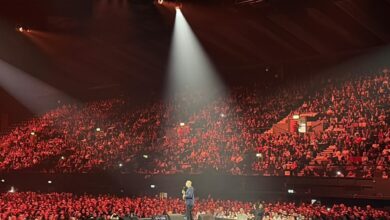 Mehdi Hasan speaking on stage at Wembley Arena during a Gaza fundraiser event, with a large audience in the background.