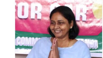 Smiling woman in traditional attire with hands folded in greeting at The Siasat Daily news event.
