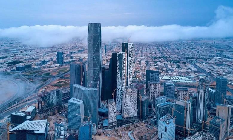 Aerial view of Riyadh city skyline with modern skyscrapers and surrounding urban landscape under cloudy sky.