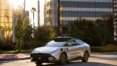 Sleek silver Tensor Robocar, a Level 4 autonomous vehicle, drives on a sunny Dubai street with lidar sensor, modern skyscrapers, and palm trees in the background.