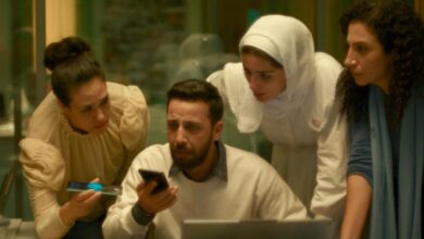 A tense scene showing three women and a man gathered closely, looking concerned at a phone screen