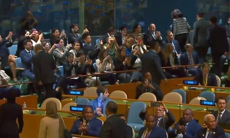 Delegates leaving the UN General Assembly hall as others clap during a session.