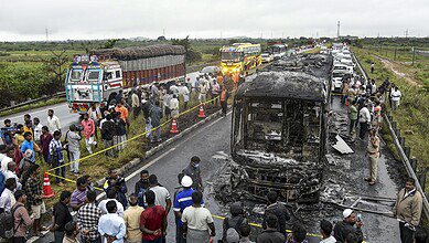 Police personnel and others gather near a Bengaluru-bound private bus that caught fire after colliding with a two-wheeler, with the blaze being triggered after the motor bike with its fuel cap open was dragged underneath the bus in Kurnool district on Friday. At least 20 people were killed in the accident. (PTI Photo)