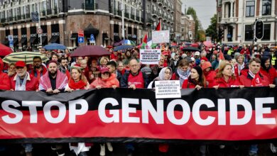 Protesters in Amsterdam wearing red hold a large banner reading “Stop Genocide” during a mass rally in solidarity with Gaza.