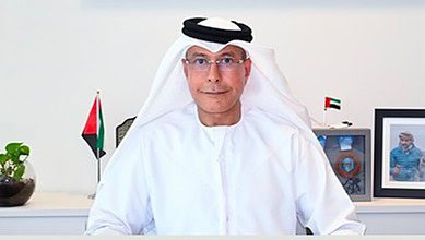 Emirati businessman and former diplomat Hamad bin Ahmed bin Salem Al Hajri seated at his desk with UAE flags and framed photo behind.