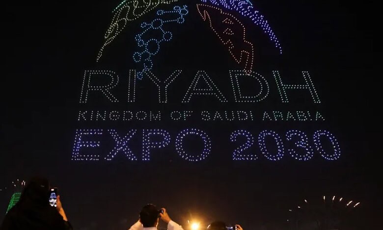 People photograph a night sky drone display forming the “Riyadh Expo 2030” logo during celebrations in Saudi Arabia.