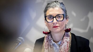 Francesca Albanese speaking at a press briefing, wearing glasses and a floral scarf.