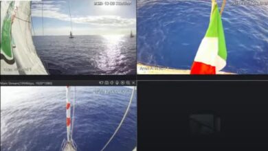 A live stream from the Freedom Flotilla shows several vessels sailing across the calm Mediterranean Sea under clear skies. One boat flies the Italian flag as sunlight reflects on the water’s surface.