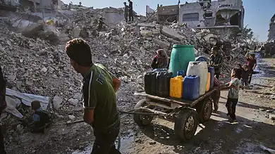 Palestinians collect and transport water through the rubble-strewn streets of Gaza City following heavy destruction.