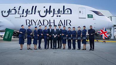 Riyadh Air flight crew and pilots pose in front of a Boeing 787 aircraft at Heathrow Airport, holding Saudi and British flags.