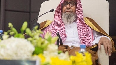 Sheikh Saleh Al-Fawzan seated during an official event, wearing a traditional Saudi robe and red-and-white ghutra.