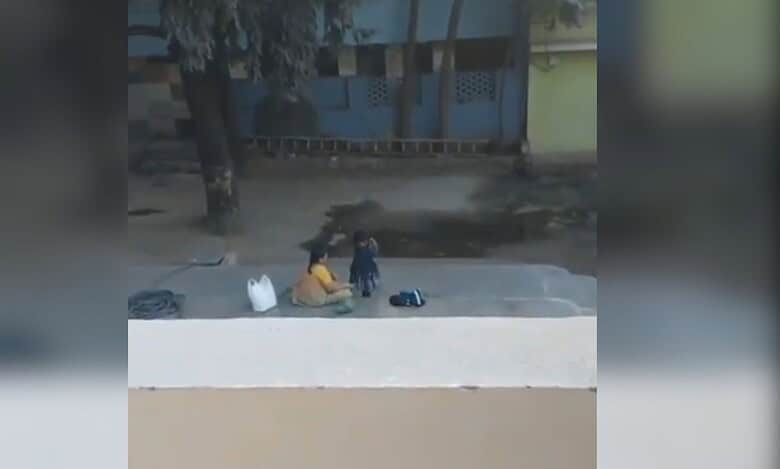 Image shows a woman dressing a young girl in a compound