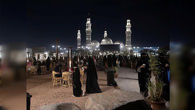 Night-time view of visitors and families at the outdoor promenade near Quba Mosque in Madinah city.