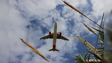 Airbus A320 flying overhead against a partly cloudy sky.