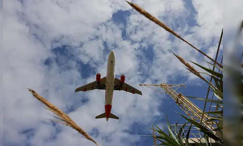 Airbus A320 flying overhead against a partly cloudy sky.