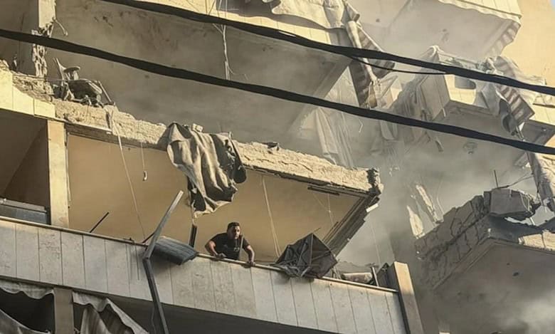 A damaged Beirut building after an Israeli airstrike, with a man standing on a shattered balcony.