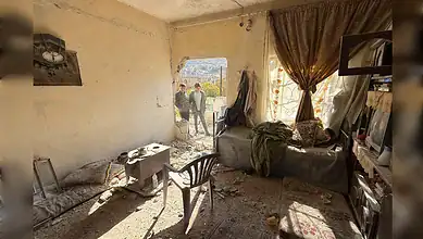 Interior of a damaged house in Beit Jinn, Syria, with two boys standing outside a hole in the wall