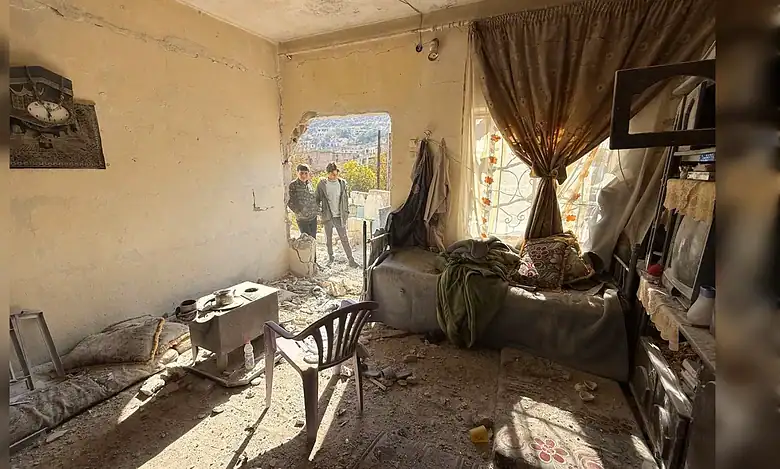 Interior of a damaged house in Beit Jinn, Syria, with two boys standing outside a hole in the wall