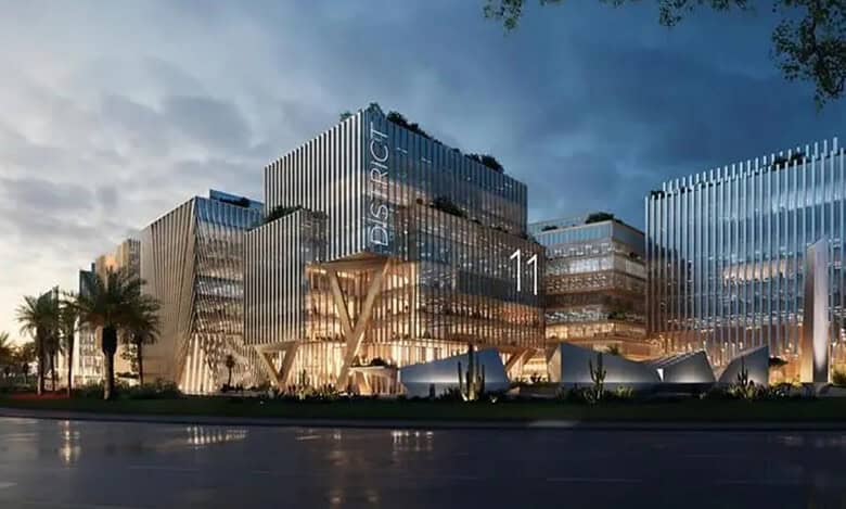 View of Al Marwan’s District 11 smart work resort in Sharjah, featuring modern glass buildings illuminated with warm lighting.