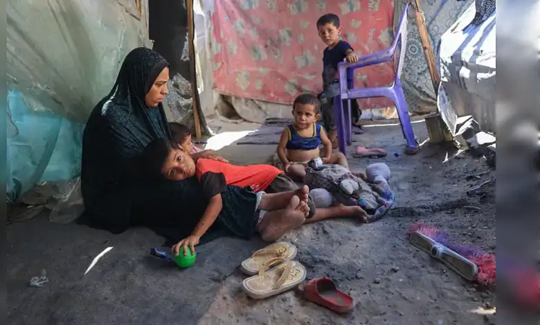 A mother sits with her young children inside a makeshift displacement shelter in Deir al-Balah during the hunger crisis in Gaza.