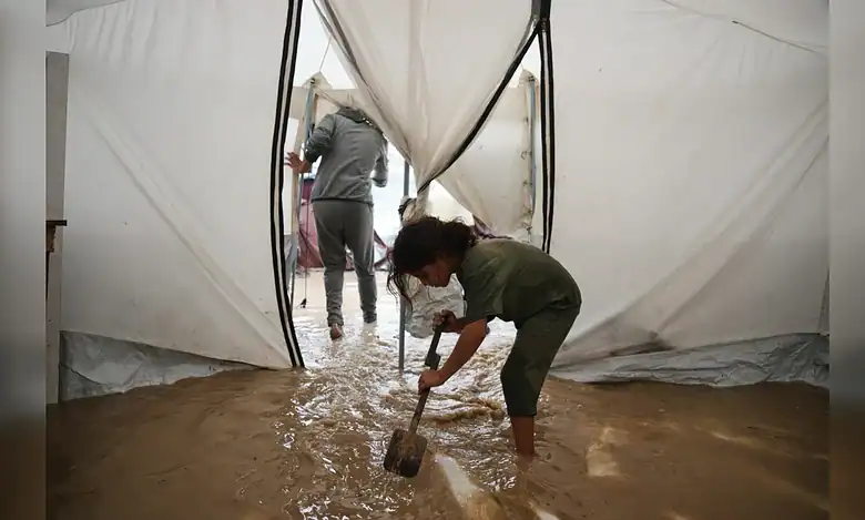 A child shovels muddy water from inside a flooded tent in Gaza.