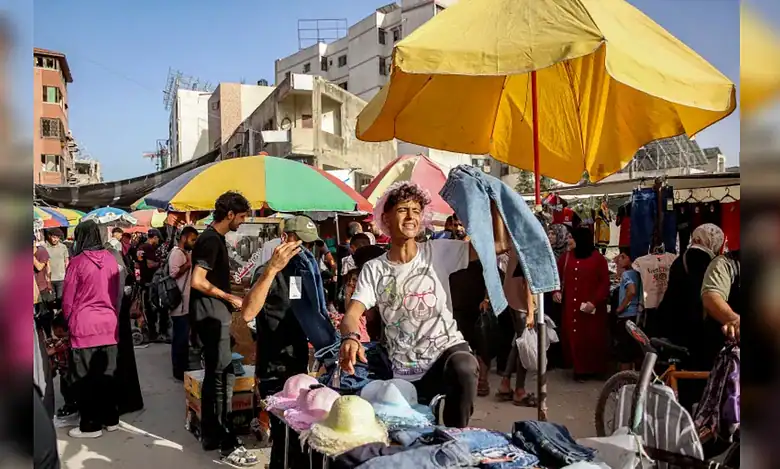A young vendor holds up trousers at a crowded outdoor market in Gaza City.