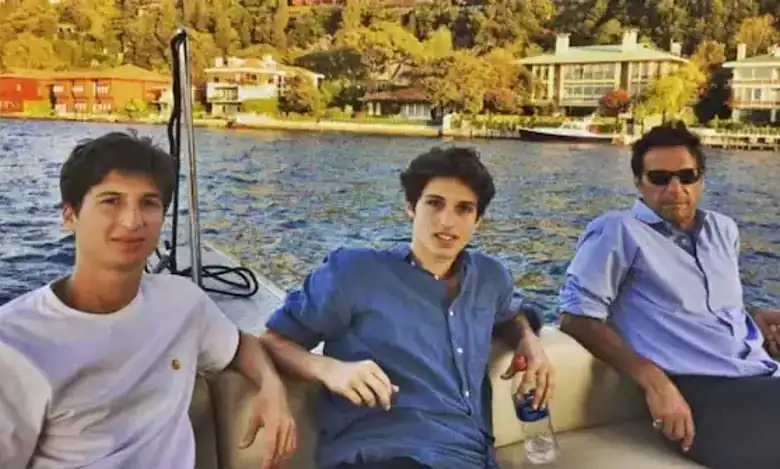Three men seated on a boat with water and houses in the background.