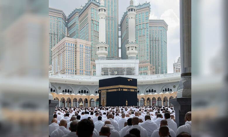 Pilgrims gathered around the Kaaba at the Grand Mosque with Makkah towers in the background.