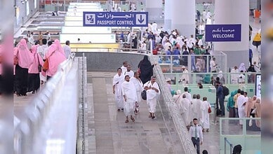 Pilgrims walking through a busy airport passport control area during Haj arrivals.