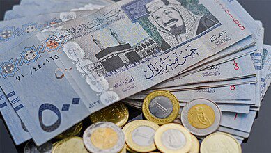 Saudi riyal banknotes and coins arranged on a table.