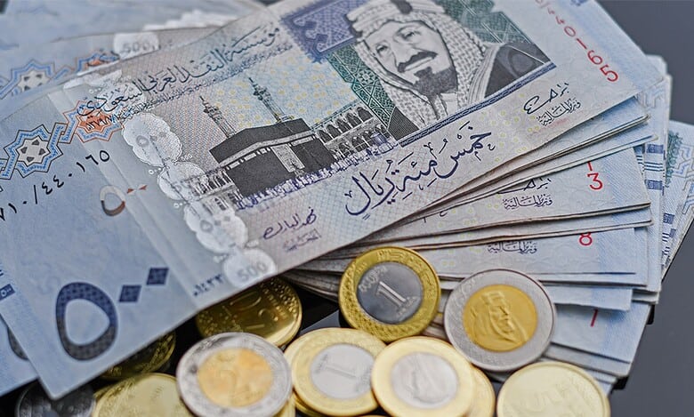Saudi riyal banknotes and coins arranged on a table.