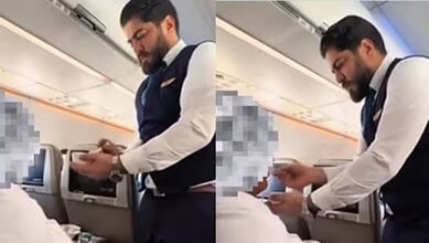 A Saudia Airlines flight cabin crew member gently feeds an elderly Umrah passenger dressed in ihram during a flight.