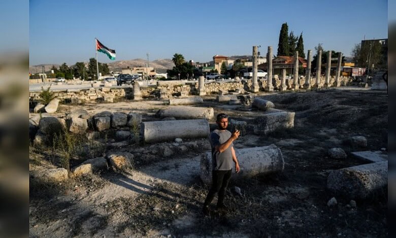 A man stands among Roman ruins in Sebastia as a Palestinian flag flies in the background.