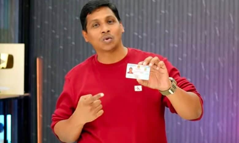 A man in a red sweatshirt holds up an identification card while speaking, with YouTube play buttons displayed in the background.