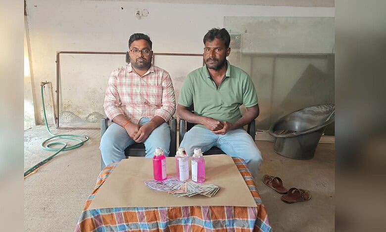 Image shows two people sitting on chairs with cash and bottles with pink liquid in front of them.