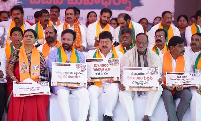 Political leaders wearing orange and green sashes sit on a stage holding signs with Telugu text and numerical figures during what appears to be a BJP party rally or demonstration.
