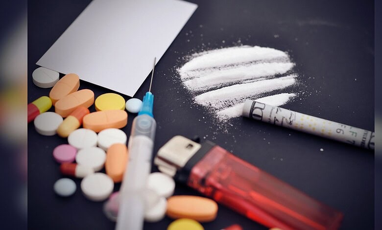 Image showing Assorted pills, a syringe, and lines of white powder with a rolled bill on a dark surface.