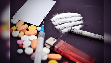 Image showing Assorted pills, a syringe, and lines of white powder with a rolled bill on a dark surface.