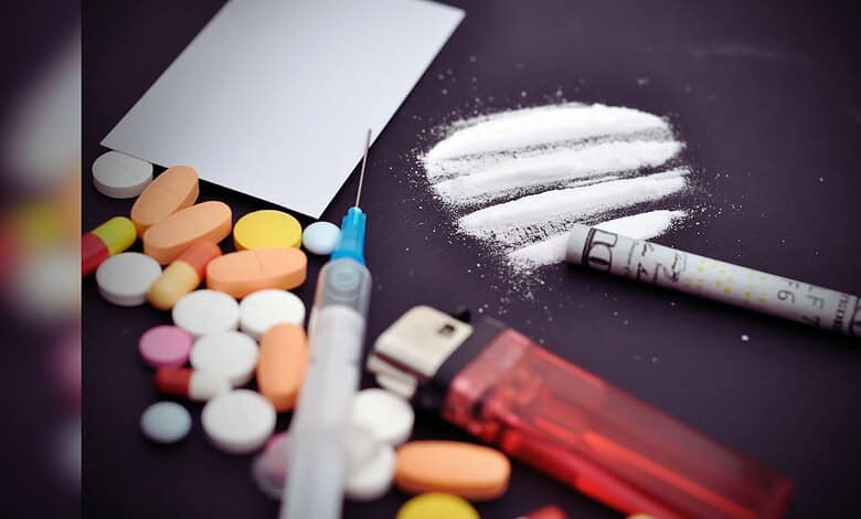 Image showing Assorted pills, a syringe, and lines of white powder with a rolled bill on a dark surface.