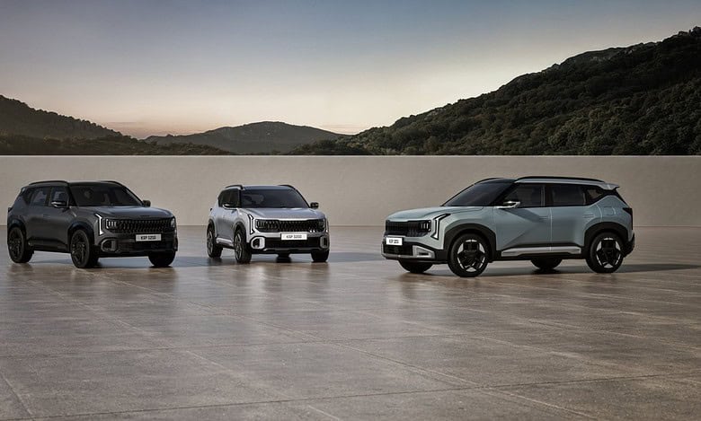 Three modern SUVs in dark gray, white, and light blue are displayed on a flat surface with rolling hills in the background at dusk.