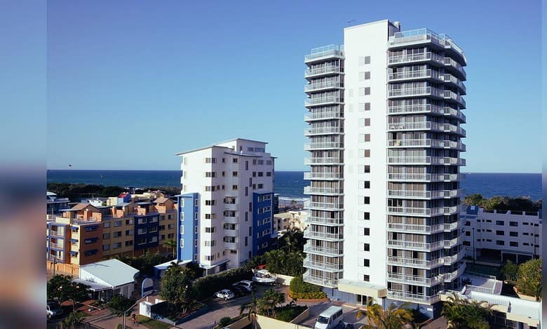 Modern white high-rise residential tower with curved balconies overlooking the ocean in a coastal urban setting