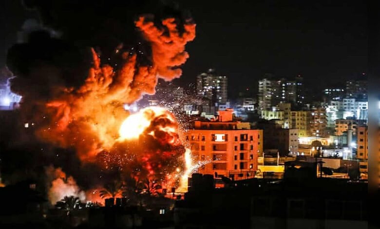 Explosion lights up buildings during Israeli air strike in Gaza City at night.