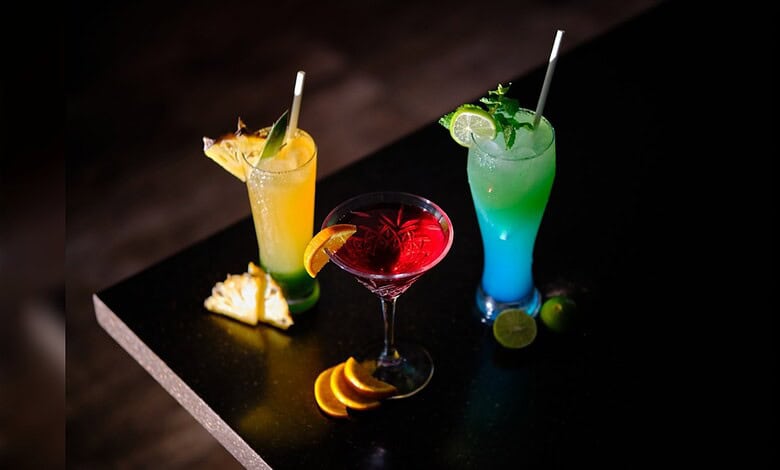Glasses of colourful sweetened beverages served with fruit garnishes.