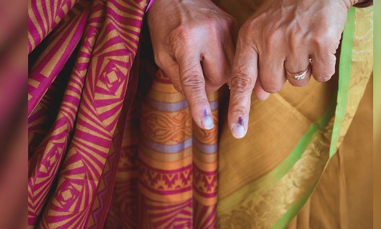 image shows two people wearing a colorful traditional sari and displaying fingers marked with ink, indicating they have voted in an election.