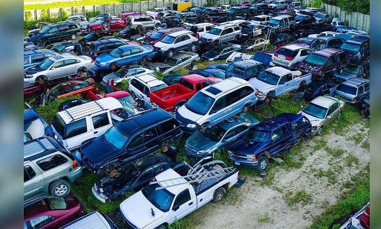 Image shows Aerial view of a densely packed salvage yard filled with various damaged and end-of-life vehicles in multiple colors.